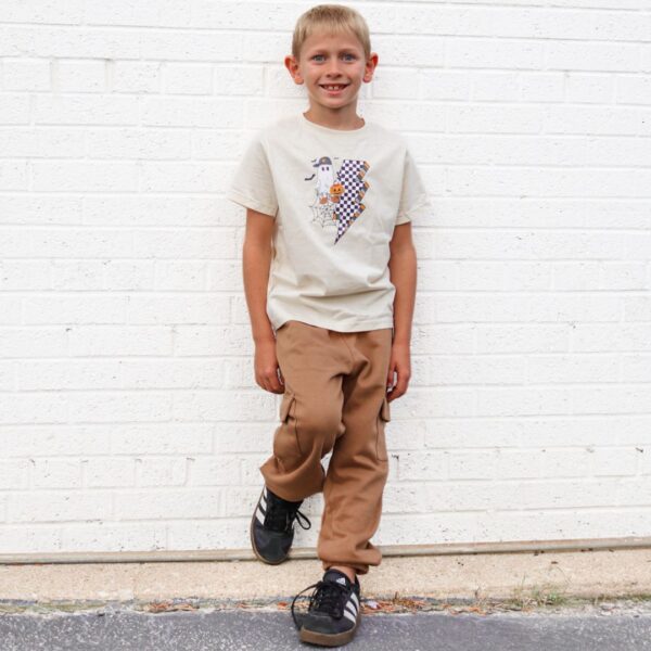 sweet wink checkered ghost halloween tee on beige Smiling child in patterned shirt and tan pants.
