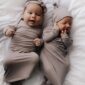 Two smiling babies in matching beige outfits.