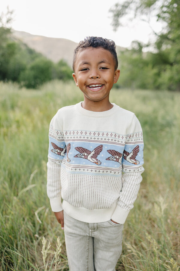 velvet fawn rylee sweater mallards Child smiling in nature, wearing bird-patterned sweater.