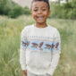 Child smiling in nature, wearing bird-patterned sweater.