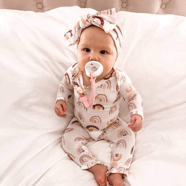itzy ritzy sweetie soother™ pacifier sets (2 pack): agave + succulent cables Baby in rainbow pajamas with pacifier on bed.