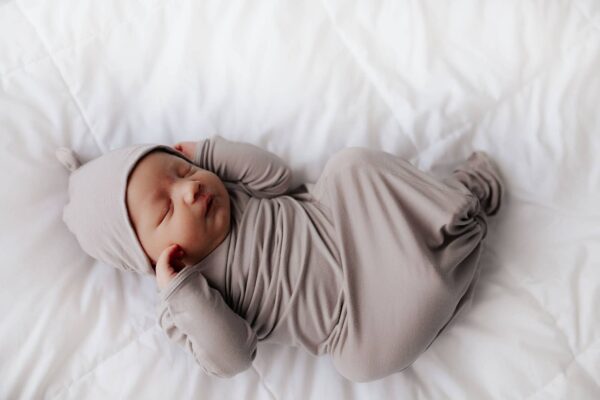 three little tots harbor mist taupe knotted gown Sleeping newborn baby in gray outfit on bed.