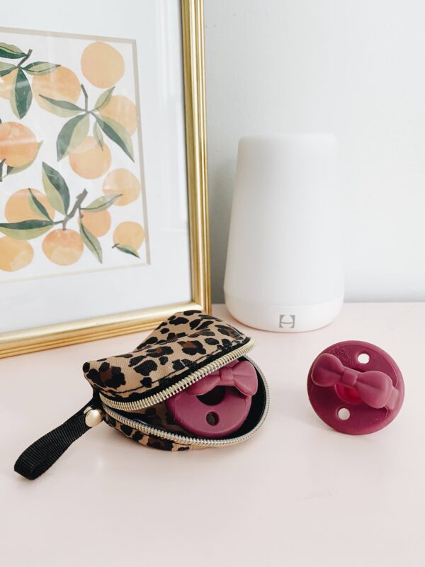 itzy ritzy sweetie soother™ pacifier sets (2 pack): aquamarine + peach bows Pacifiers in leopard case beside white diffuser.