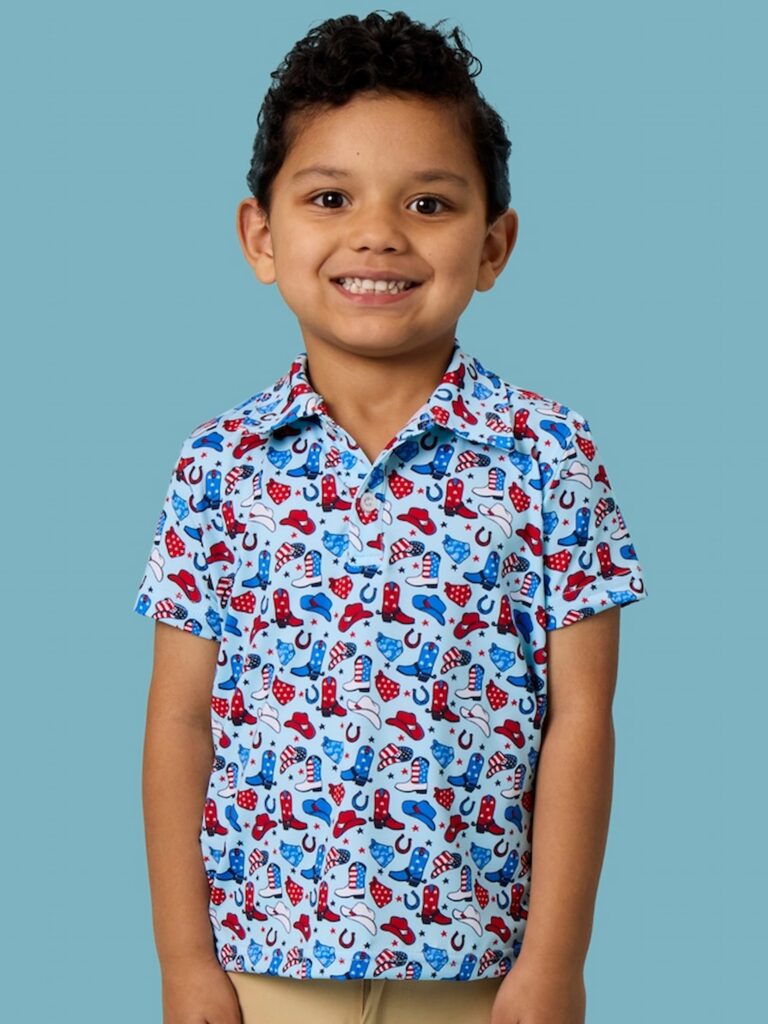 Young boy wearing red, white, and blue stars and spurs RuggedButts polo on a blue background.