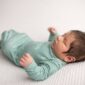 Newborn baby in green outfit sleeping peacefully.