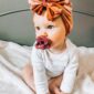 Baby with headwrap and pacifier on blanket.