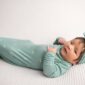 Baby in teal outfit lying on white blanket.