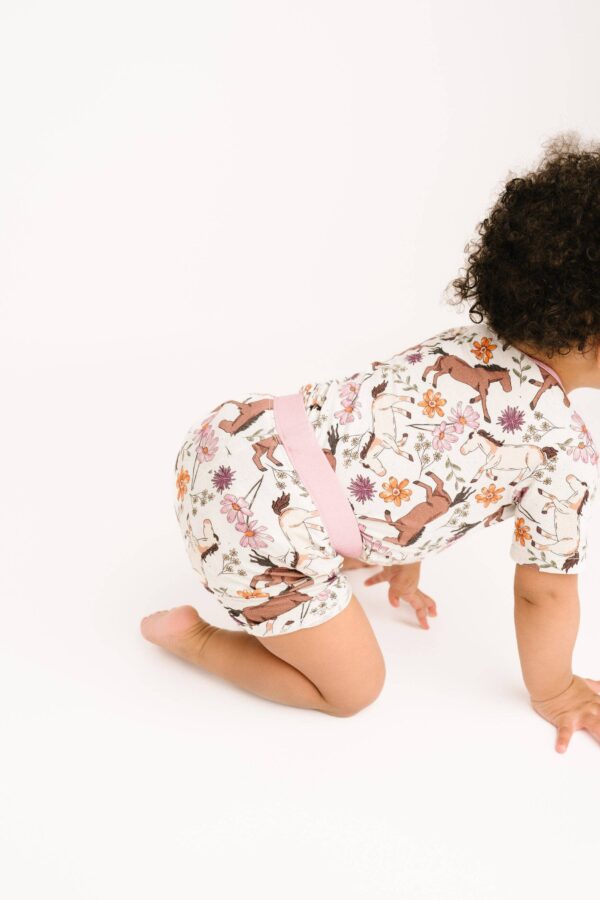 little one shop prairie ponies bamboo shorts set Baby crawling in floral romper, white background.