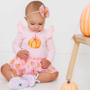 Baby in pink pumpkin outfit sitting on floor.