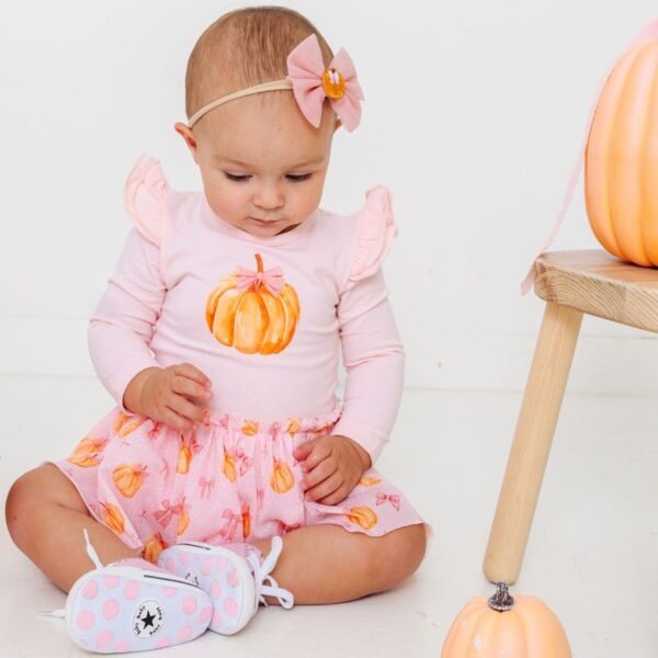 Baby in pink pumpkin outfit sitting on floor.