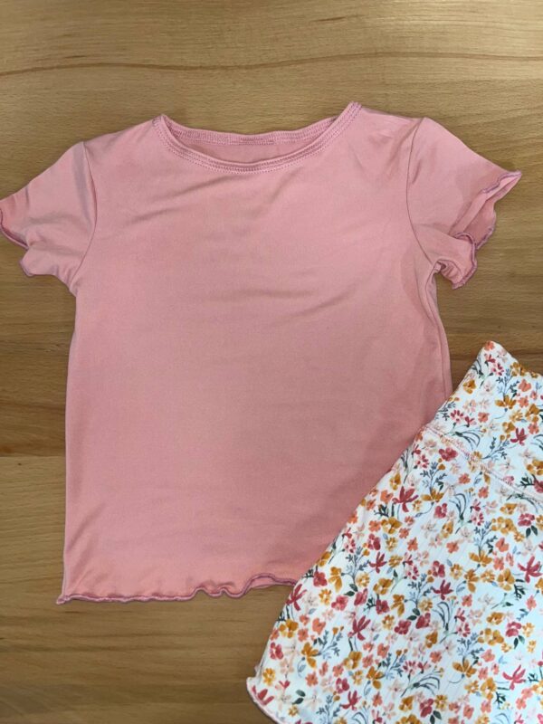 Pink shirt with floral skirt on wooden surface.
