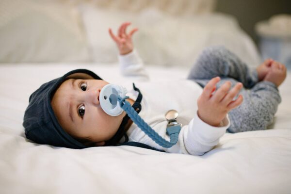 itzy ritzy sweetie soother™ pacifier sets (2 pack): agave + succulent cables Baby lying with pacifier on bed, looking up.