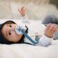 Baby lying with pacifier on bed, looking up.