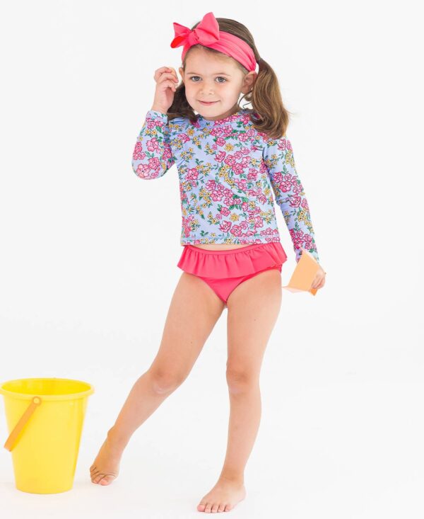 rufflebutts cheerful blossoms princess seam ruffle rash guard 2 piece Girl in floral swimsuit with bucket and spade.