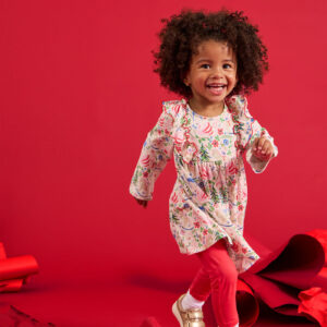 Smiling child wears colorful floral dress, red background.