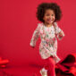 Smiling child wears colorful floral dress, red background.