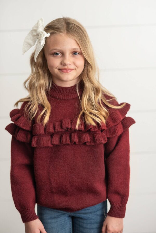 oopsie daisy kids wine double ruffle crew neck fall winter sweater Girl in red sweater with ruffles smiling indoors.