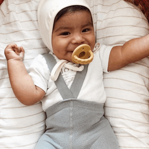itzy ritzy sweetie soother™ pacifier sets (2 pack): agave + succulent cables Smiling baby with pacifier in cozy outfit.