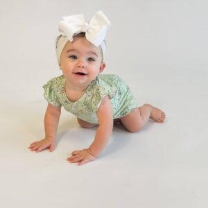 Baby crawling with white bow and floral romper.