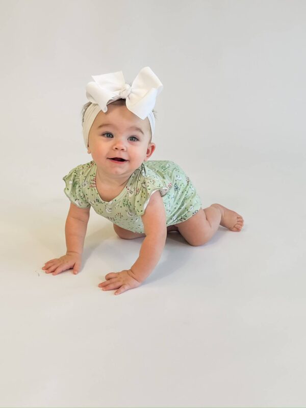 Baby crawling with white bow and floral romper.