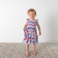 Child in floral dress, standing on rug.