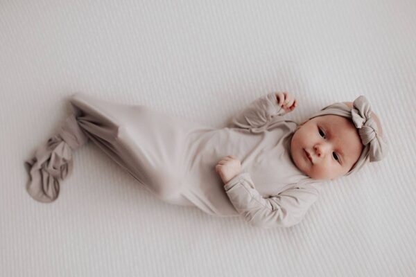 three little tots harbor mist taupe knotted gown Baby in beige outfit lying on white blanket.