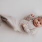 Baby in beige outfit lying on white blanket.