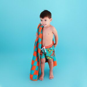 Child with towel and swim trunks on blue background.