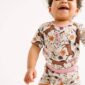 Smiling baby in floral horse-patterned outfit.