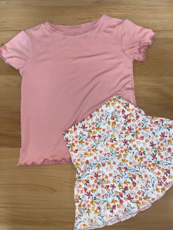 yoga baby peach short sleeve lettuce edged tee Pink shirt and floral skirt set on wood floor.