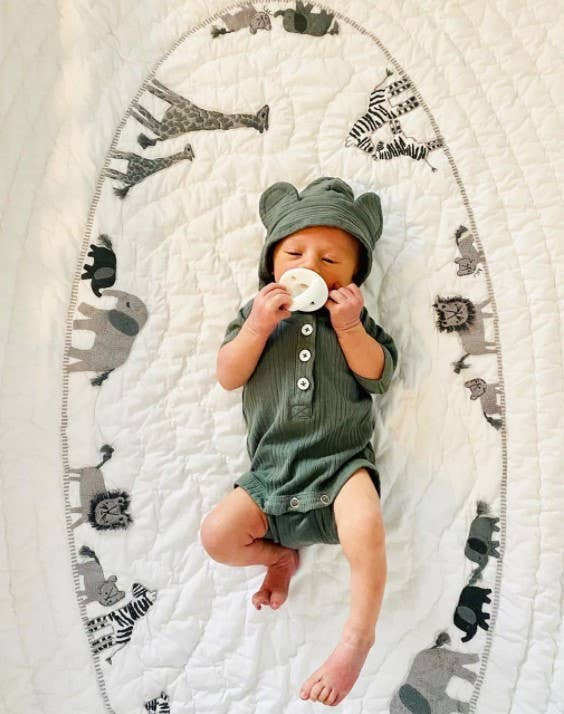 itzy ritzy sweetie soother™ pacifier sets (2 pack): toast + buttercream braids Baby in green onesie on animal-patterned blanket.