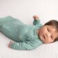 Newborn baby in green outfit on white blanket.