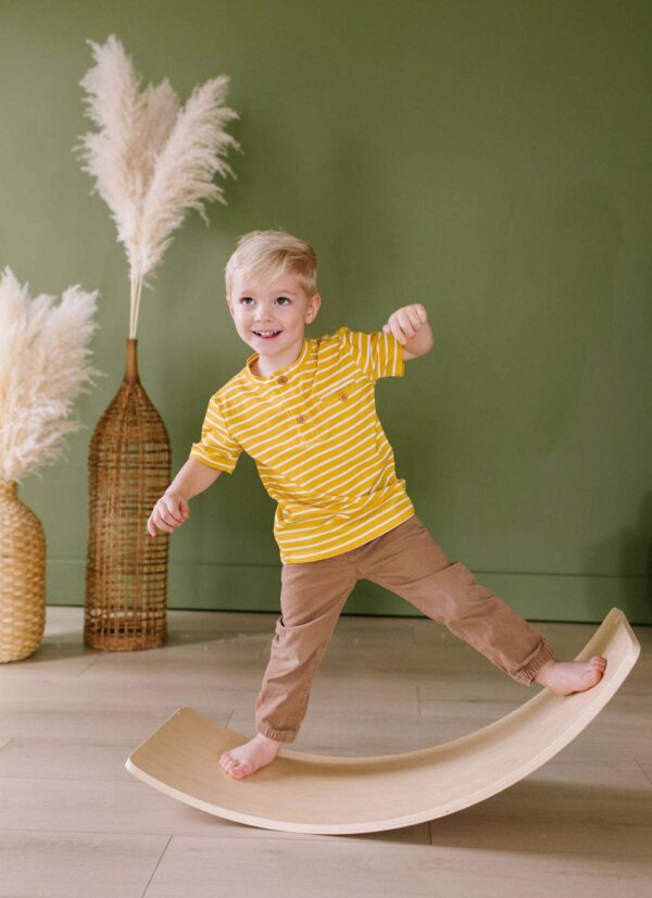 ollie jay alex tee in mustard stripe Child balancing on wooden board in striped shirt.