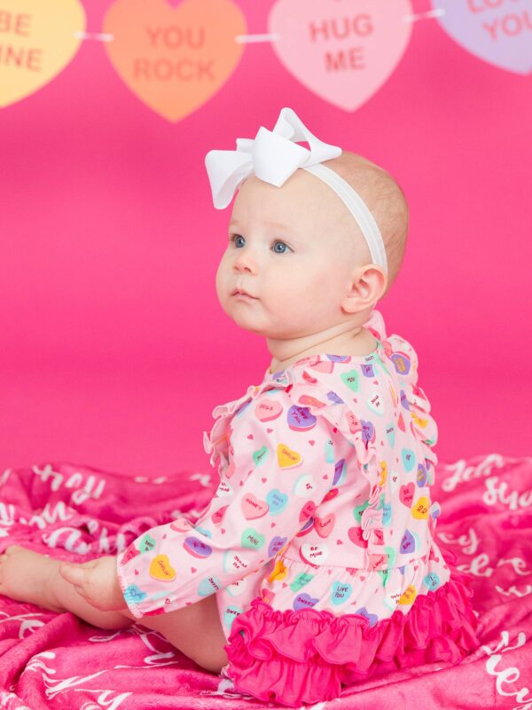 rufflebutts + ruggedbutts baby girls be my valentine knit long sleeve waterfall bubble romper Baby in colorful outfit with candy hearts background.