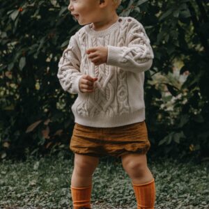 Toddler in sweater outdoors, standing on gravel path.