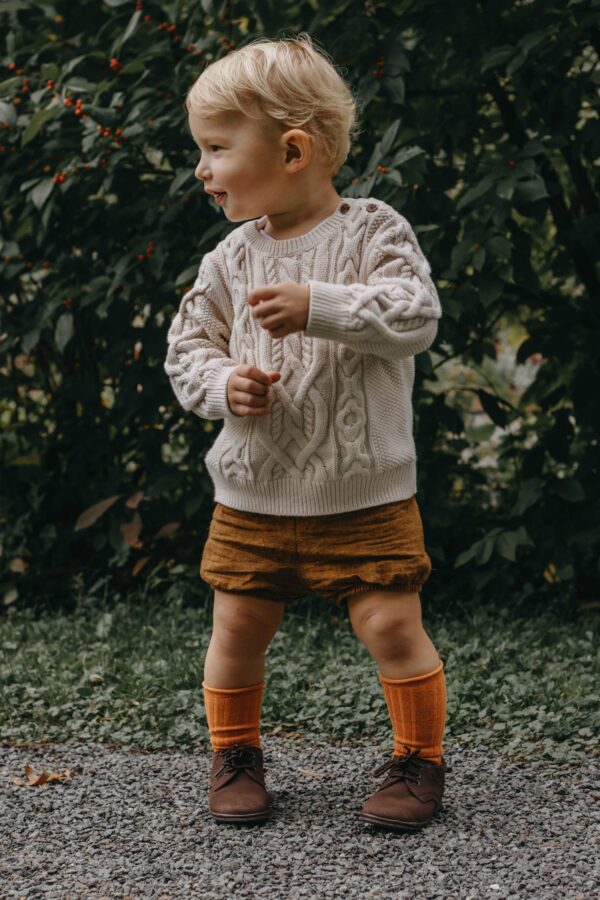 angel baby nubuck brown suede oxford shoe Toddler in sweater outdoors, standing on gravel path.