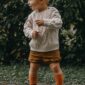 Toddler in sweater outdoors, standing on gravel path.