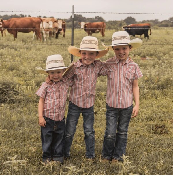 cowkid clothing co red stripe vintage pearl snap Three kids in cowboy hats standing together near cows.