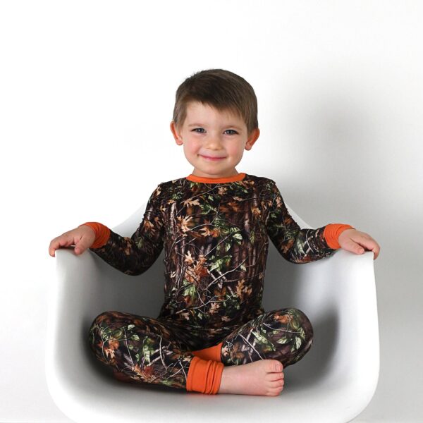 gigi and max hunter camo two piece no button bamboo outfit lounge Child wearing camo pajamas sitting on white chair.
