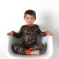 Child wearing camo pajamas sitting on white chair.
