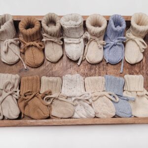 Knit baby booties on wooden tray, various colors.