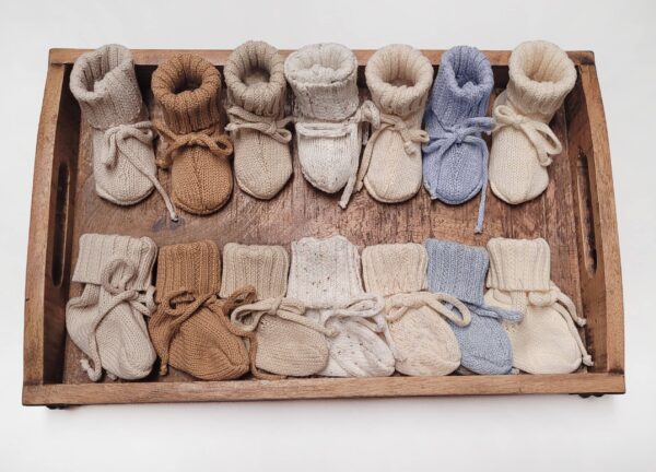 Knit baby booties on wooden tray, various colors.