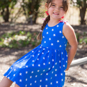 Girl in blue star-pattern dress smiling outside.