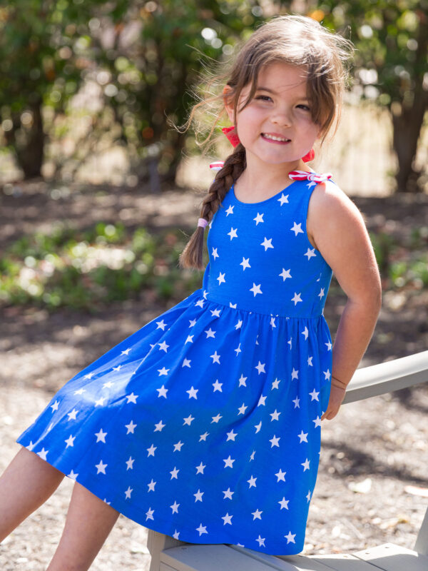 rufflebutts stars and stripes twirl tank dress Girl in blue star-pattern dress smiling outside.