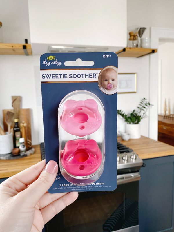 itzy ritzy sweetie soother™ pacifier sets (2 pack): agave + succulent cables Pink pacifiers in kitchen setting.