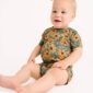 Baby in floral romper with headband, sitting.