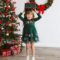 Girl in festive dress holding gift near Christmas tree.