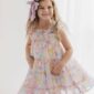Girl wearing colorful summer dress with purple bow.