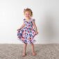 Child wearing floral dress, smiling, standing indoors.