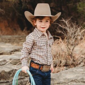 Young child wearing cowboy hat holding rope outdoors.